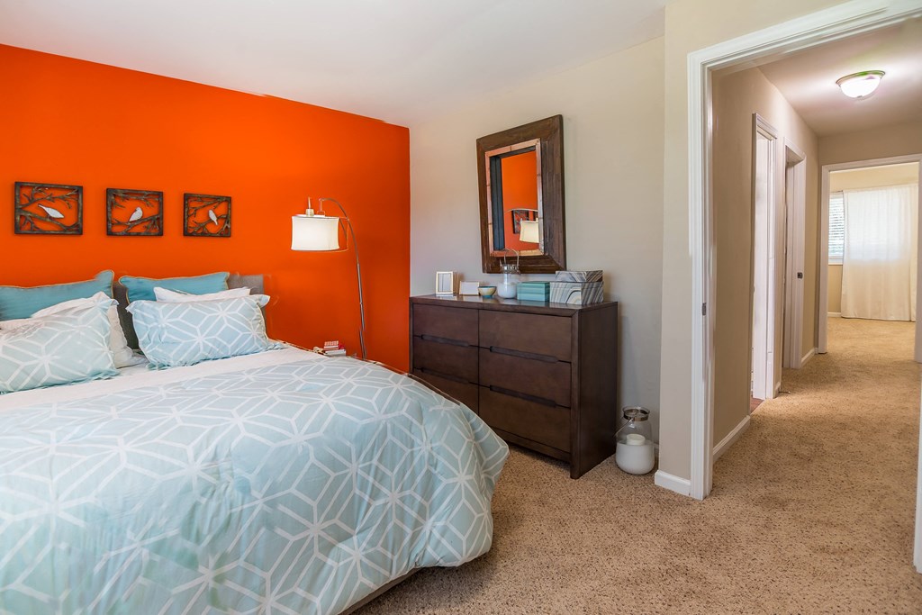 a bedroom with an orange accent wall and a large bed with a blue comforter at Broadway at East Atlanta, Atlanta, GA